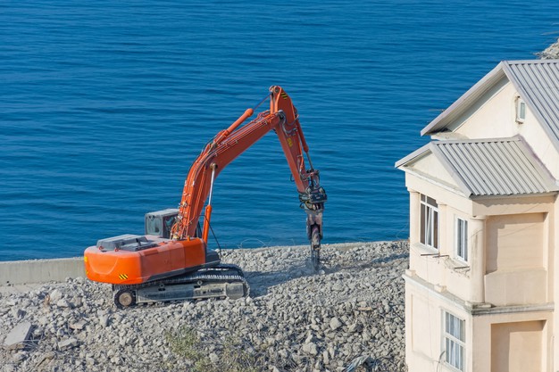 excavator-with-hydraulic-shears-against-demolished-building-dismantling-emergency-construction-standing-seashore_165577-525