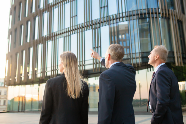 group-business-partners-formal-suits-pointing-office-building-meeting-outdoors-discussing-real-property-back-view-commercial-real-estate-concept_74855-7313