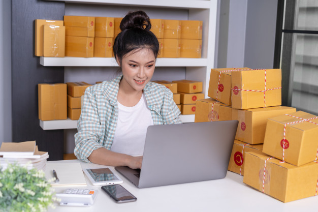 happy-woman-working-with-laptop-computer-courier-parcel-box-home-office_35076-3030