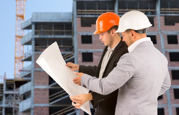 two-architects-engineers-standing-discussing-building-blueprint