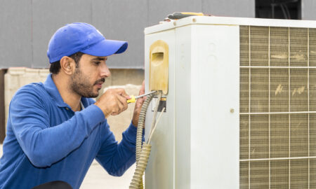 a professional electrician man is fixing a heavy duty unit of central air conditioning system by his tools on the roof top and wearing grey color of uniform and white cap